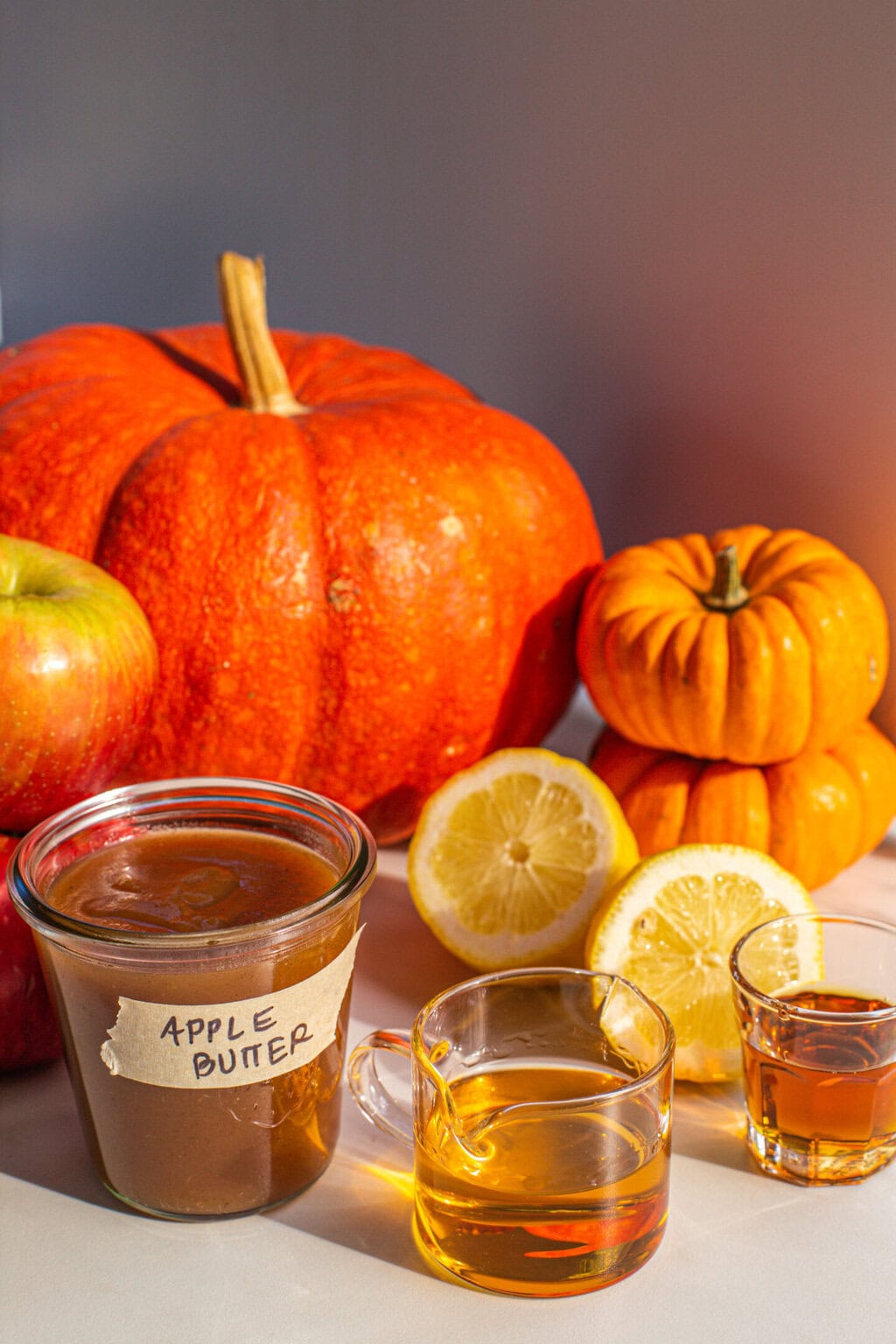 a glass jar of apple buter, maple syrup, apple juice, fresh lemons and decorative pumpkins