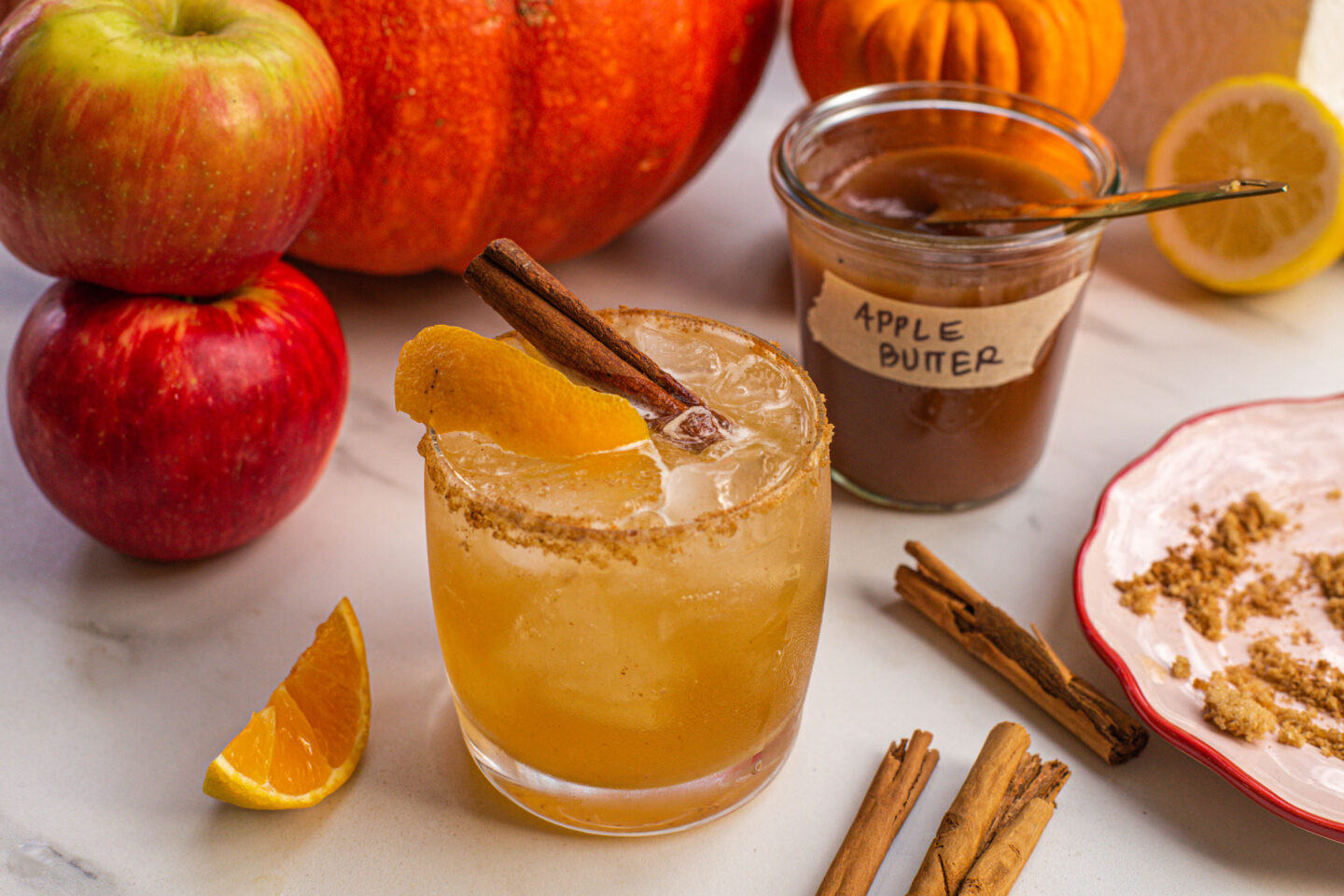 a whiskey cocktail in a low glass with a jar of apple butter and apples next to it