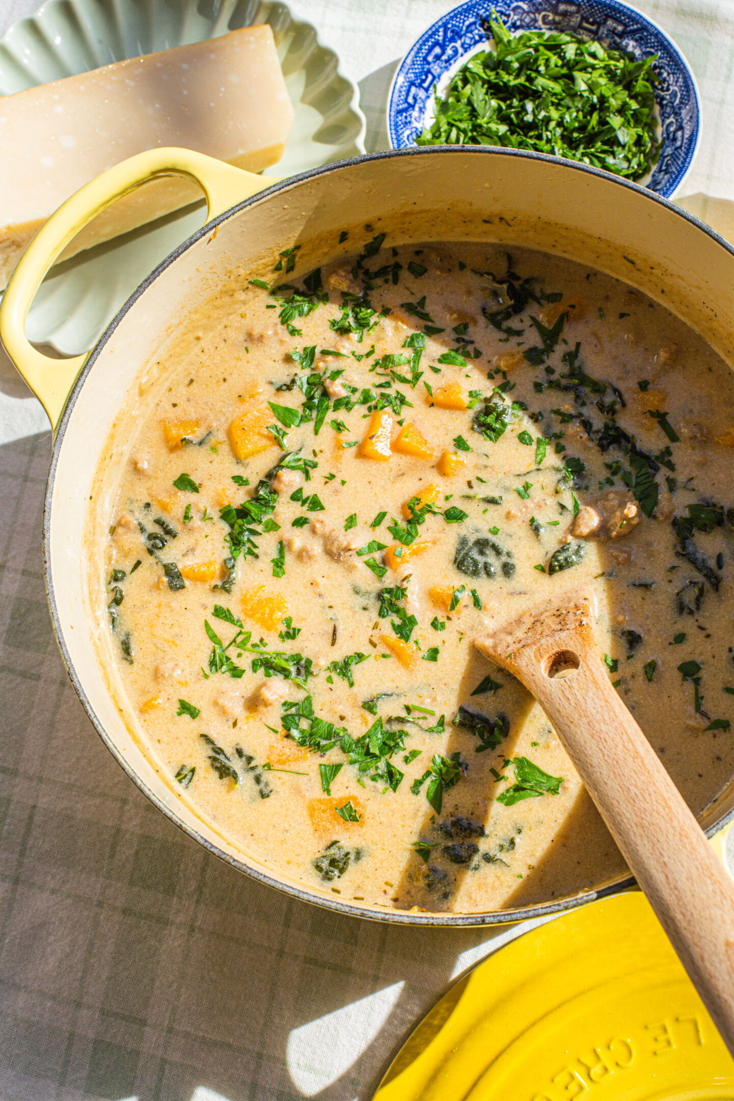 a yellow dutch oven filled with creamy Italian gnocchi soup and a small bowl of parsley and a wedge of Parmesan cheese