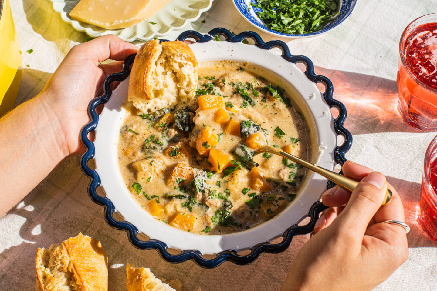 a bowl of soup in a blue. and white dish with two hands, a golden spoon and a piece of bread