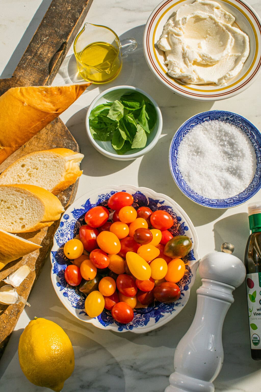 baguette and slices, olive oil, fresh basil leaves, ricotta cheese, kosher salt, cherry tomatoes, pepper mill, balsamic glaze, lemon