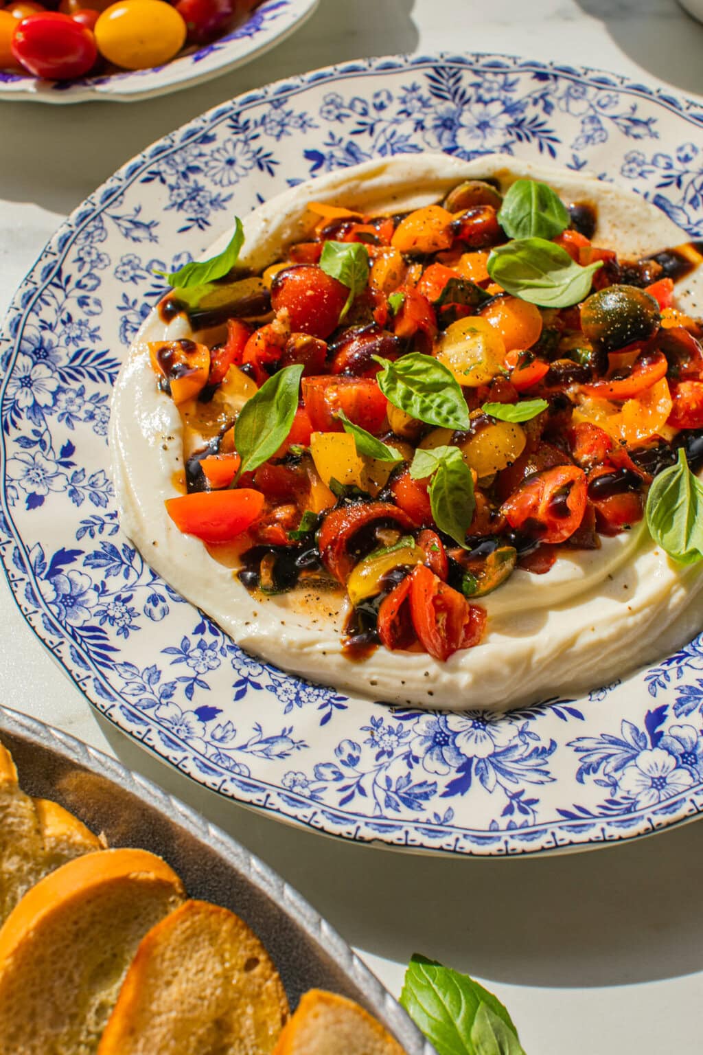 blue and white platter with whipped ricotta and bruschetta dip topper with tomatoes, basil and balsamic glaze
