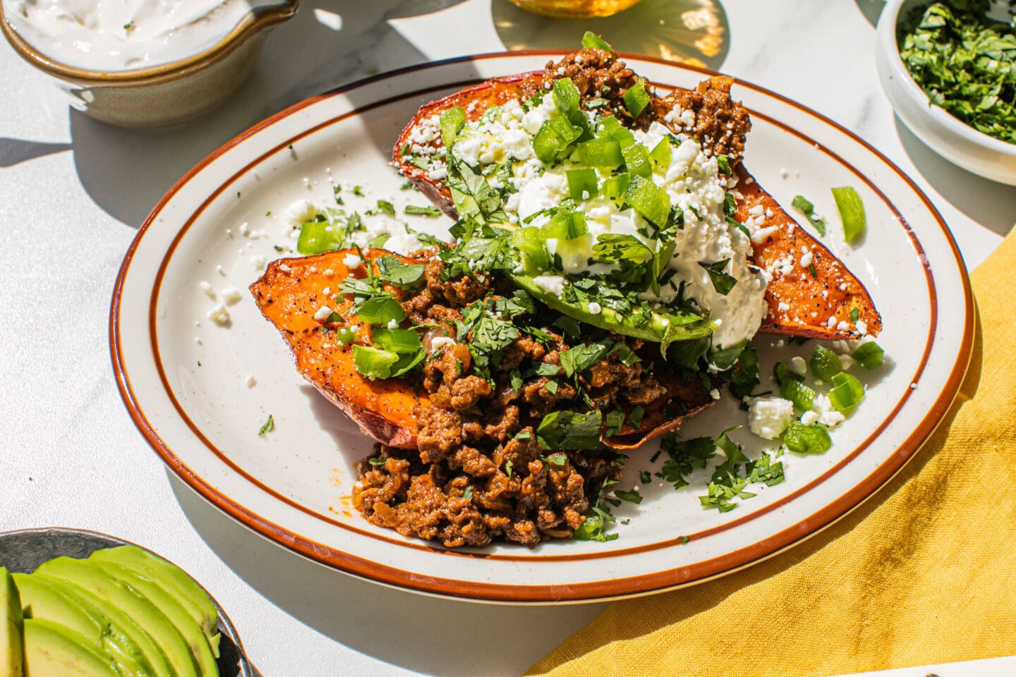 bowl of feta cheese, bowl of sour cream, bowl of jalapenos, sweet potato and ground beef on a plate with brown lines, yellow napkin