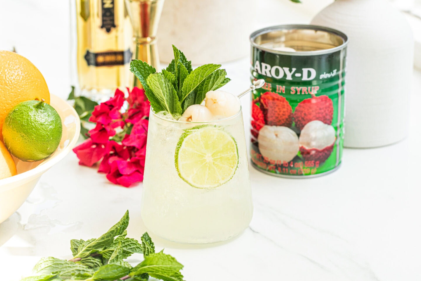 bowl of citrus, a glass of lychee cocktail spritz, can of lychees, st germain bottle