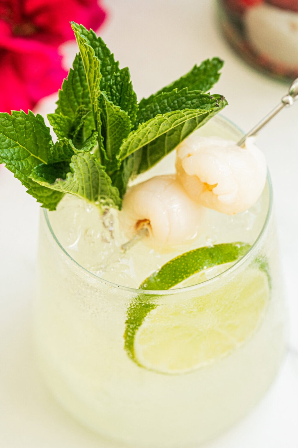 a stemless wine glass with lychee cocktail spritz, two lychee fruits, a sprig of fresh mint and a lime wheel