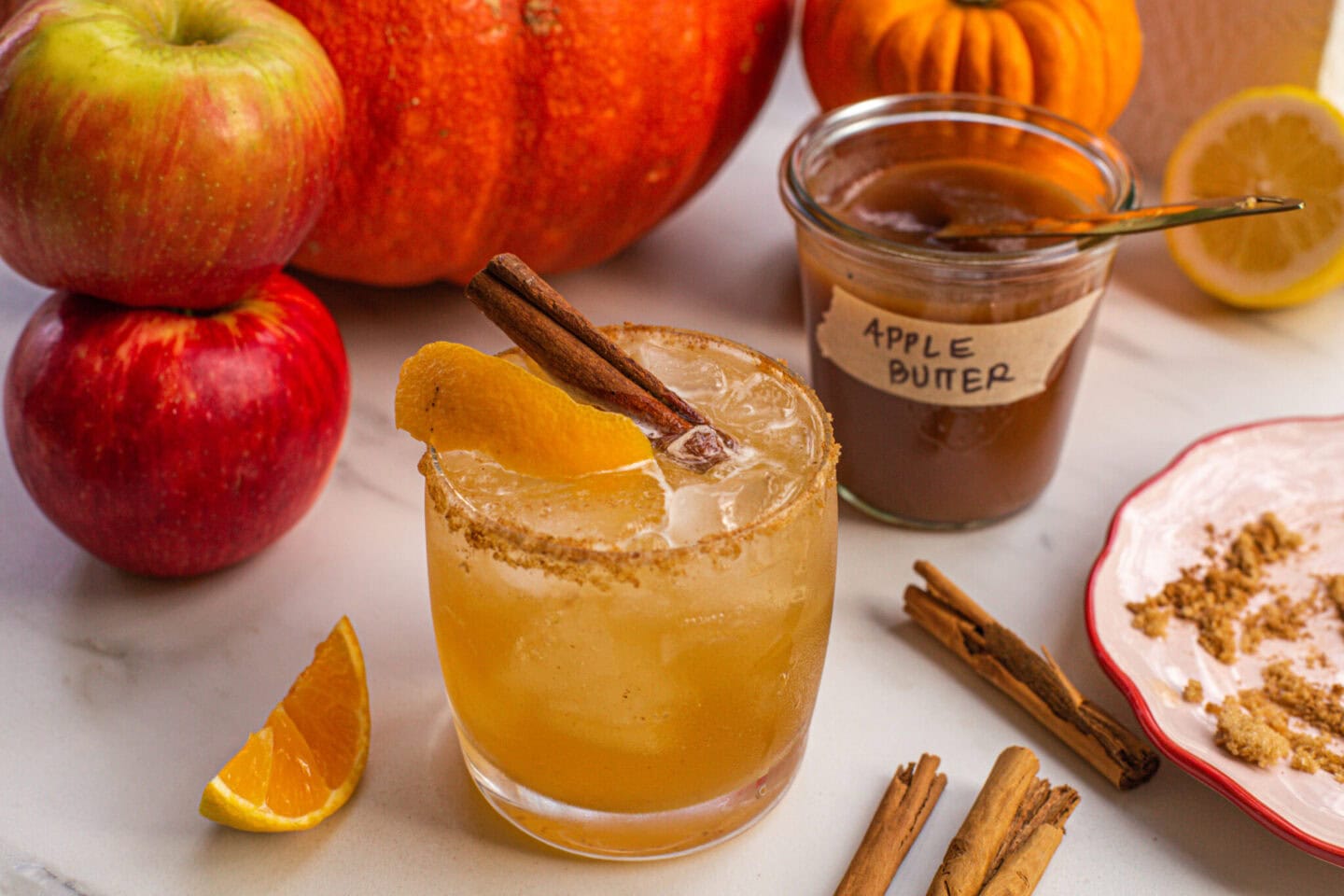 an apple bourbon drink a rocks glass garnished with an orange peel and a cinnamons tick