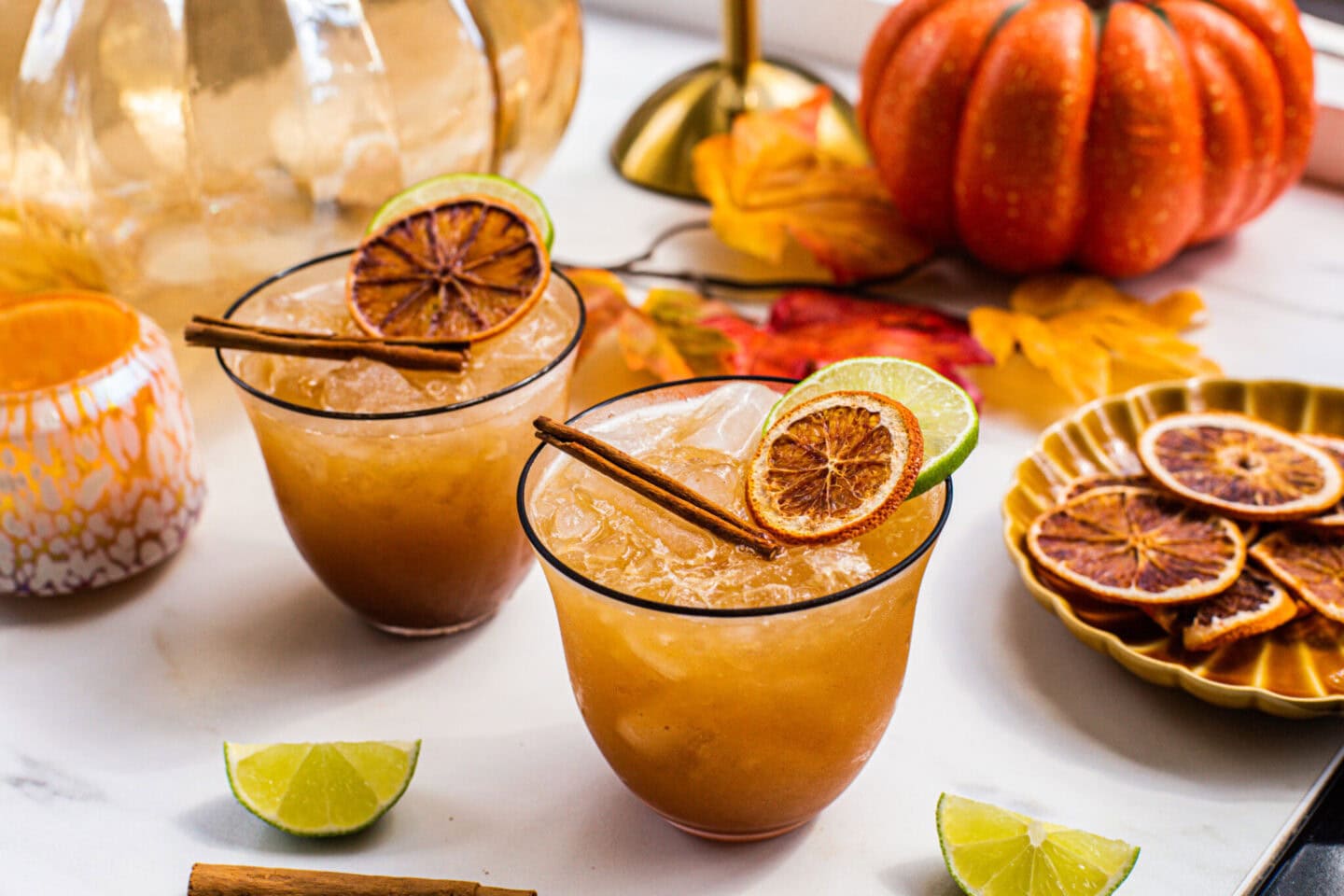 a pumpkin spice margarita in a glass with a black rim, garnished with a dehydrated orange, lime wheel and cinnamon stick