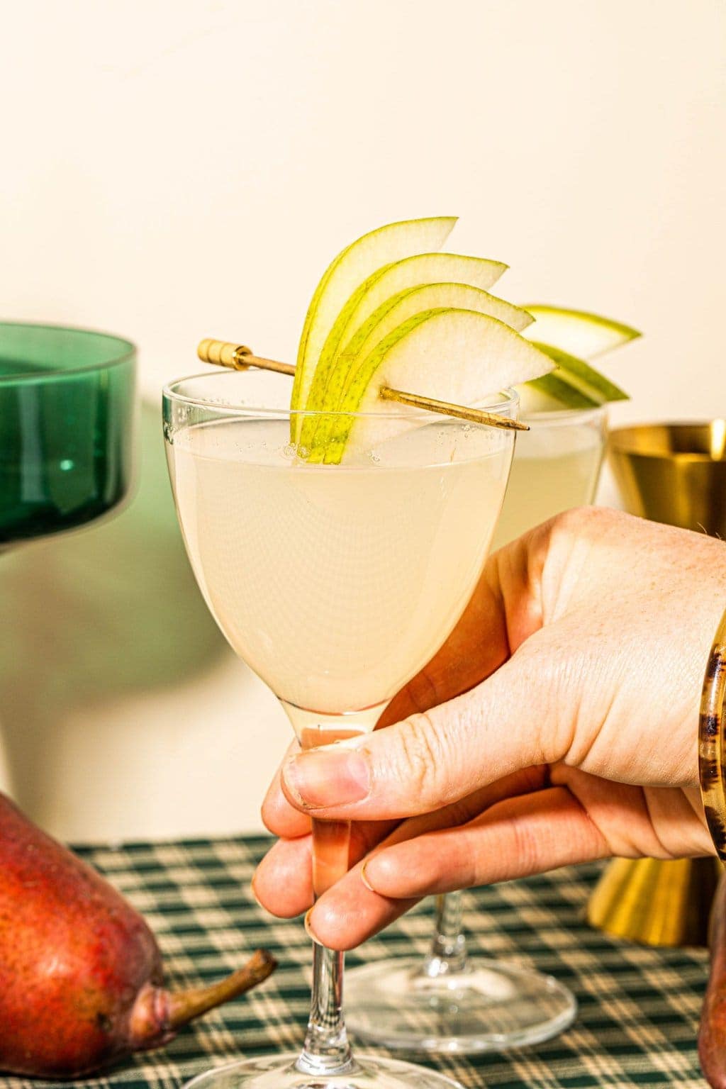 a pear martini garnished with a fan of pear slices on a cocktail pick with a hand holding the drink