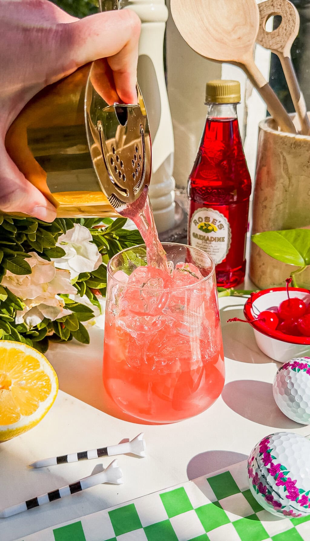 azalea cocktail being poured from a gold cocktail shaker and strainer into a glass filled with ice
