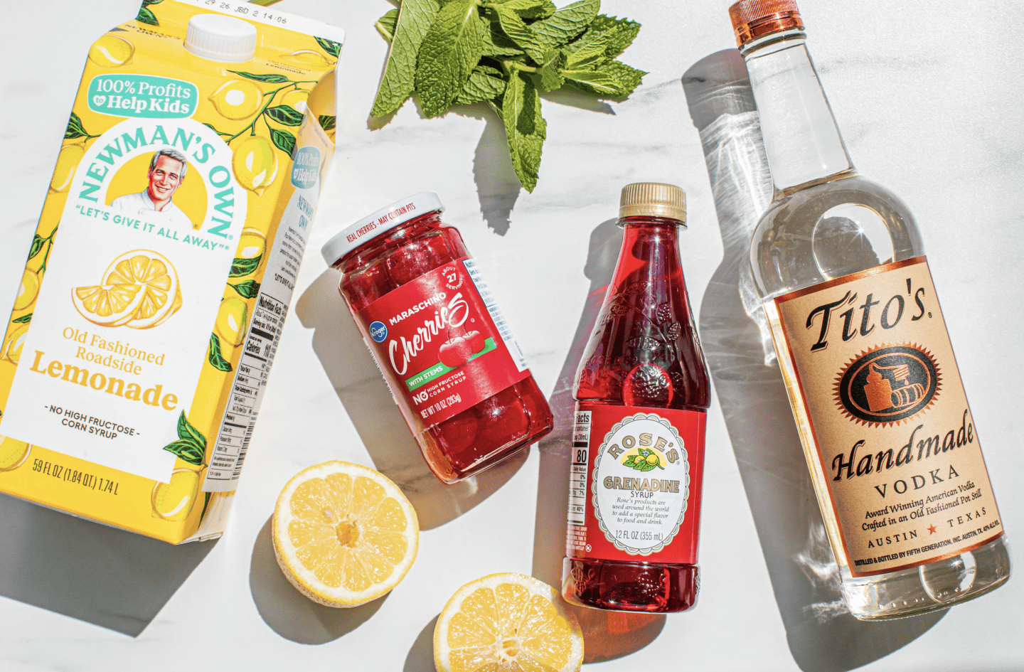 carton of Newman's Own lemonade, a glass jar of maraschino cherries, a bottle of grenadine, a handle of tito's vodka
