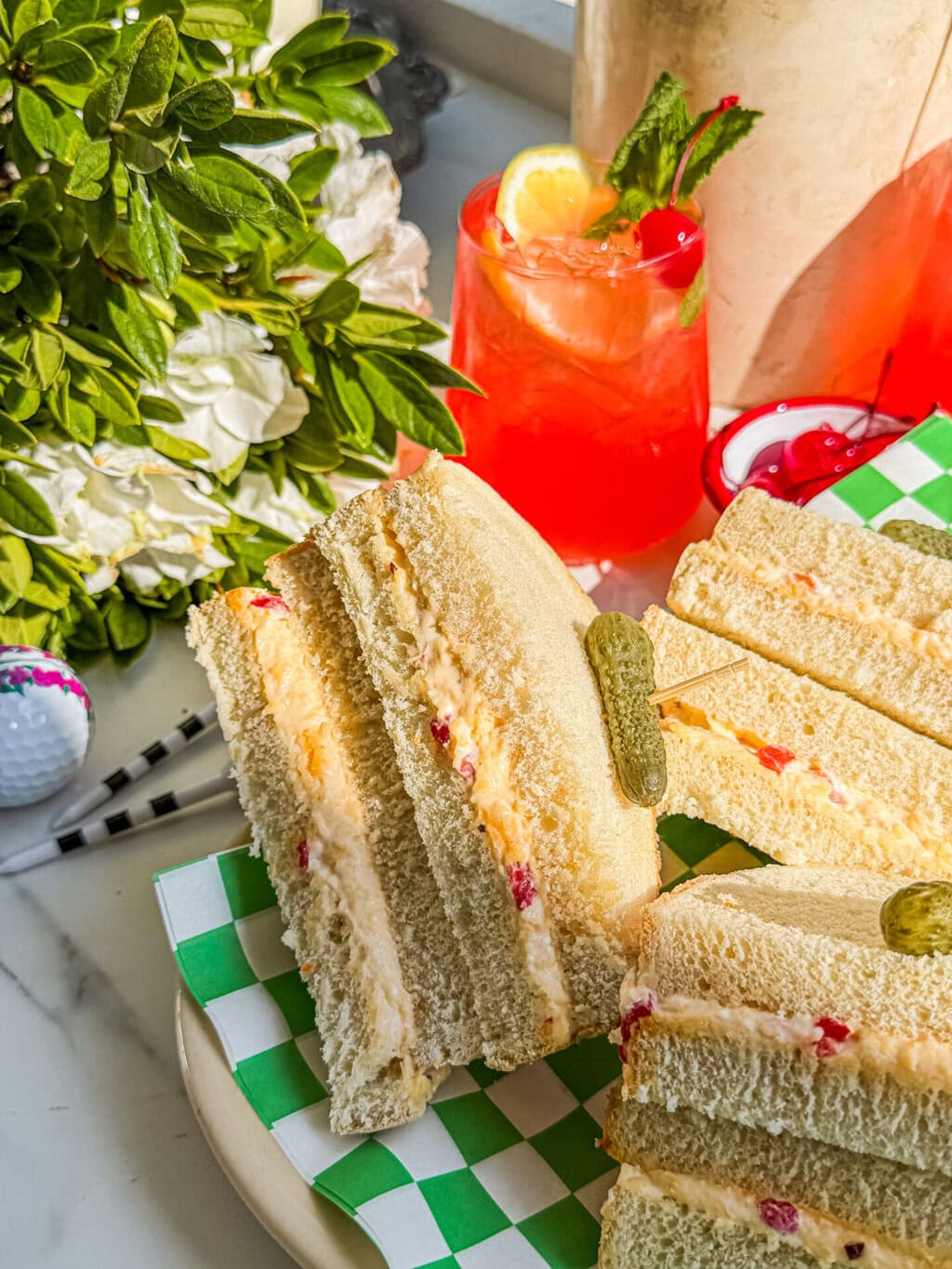 a few slices of pimento cheese sandwich, an azalea cocktail, a bush of azalea flowers and a few golf balls