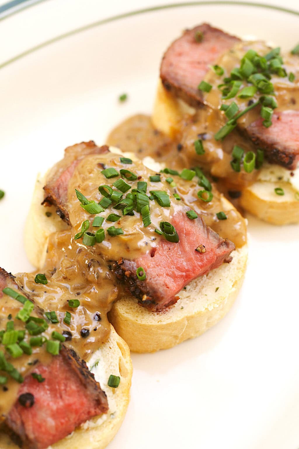 three crostinis topped with boursin, steak slice, au poivre sauce and chopped chives