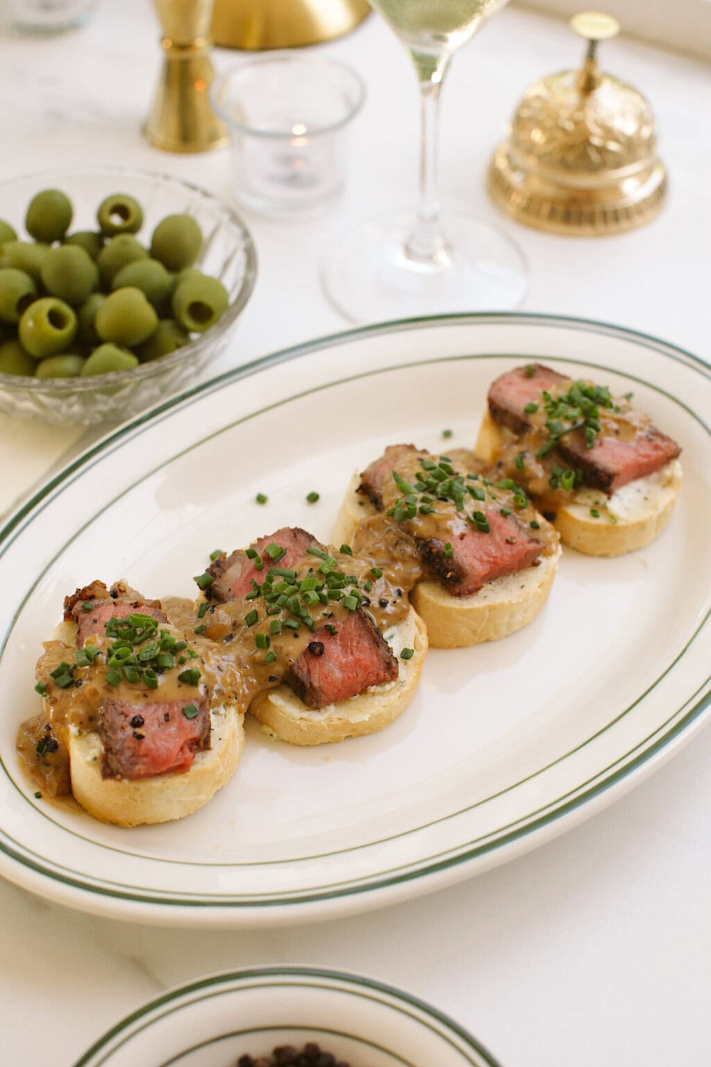 a green striped serving platter topped with four steak crostinis