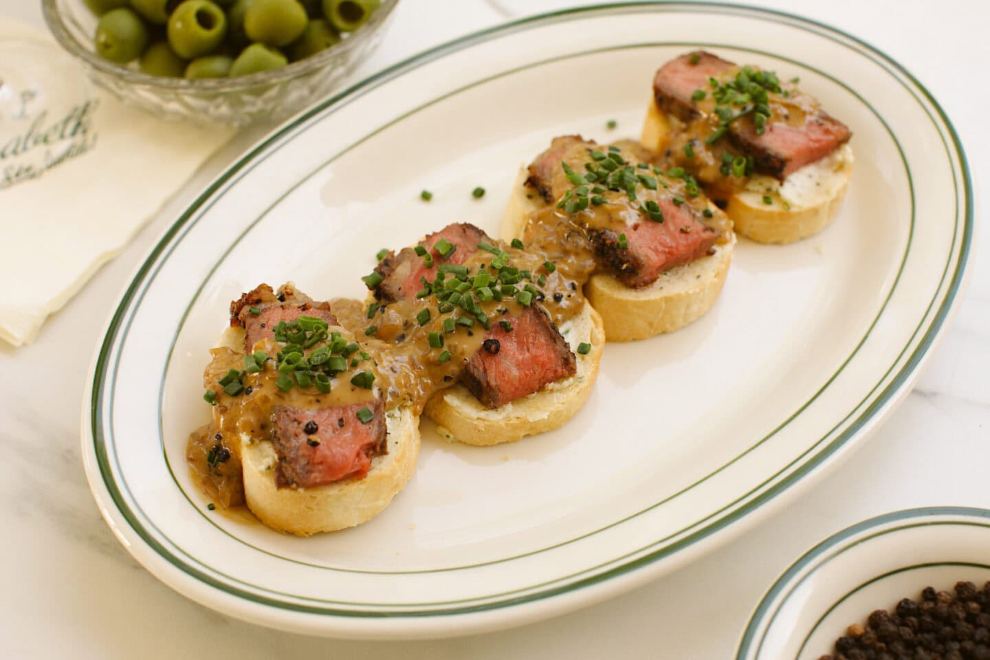 a green striped oval platter topped with four steak crostinis