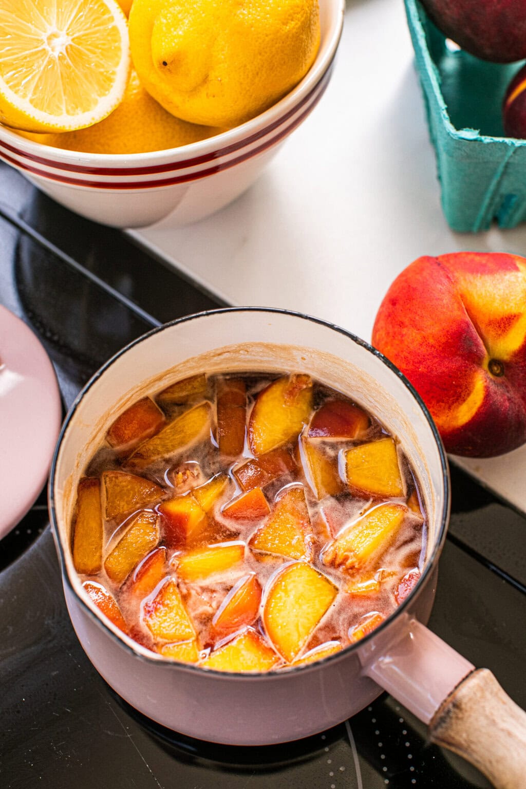 peach honey syrup on the stove in a small pink pot with a whole peach next to it